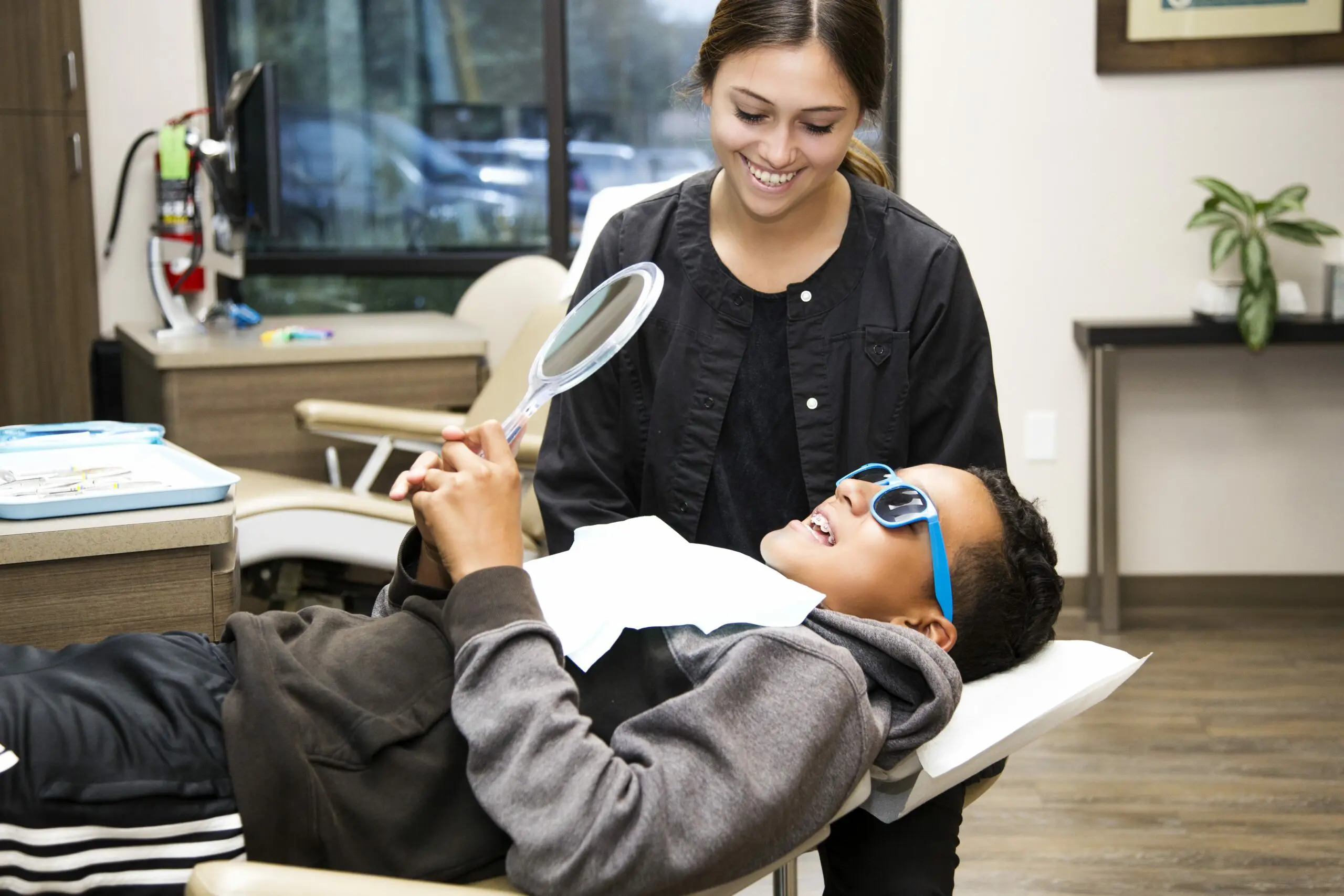 A smiling child with sunglasses holds a mirror as a dental professional explains the Orthodontic Appliances during a free orthodontic consultation at Gianquinto Orthodontic Arts in Bakersfield, CA.
