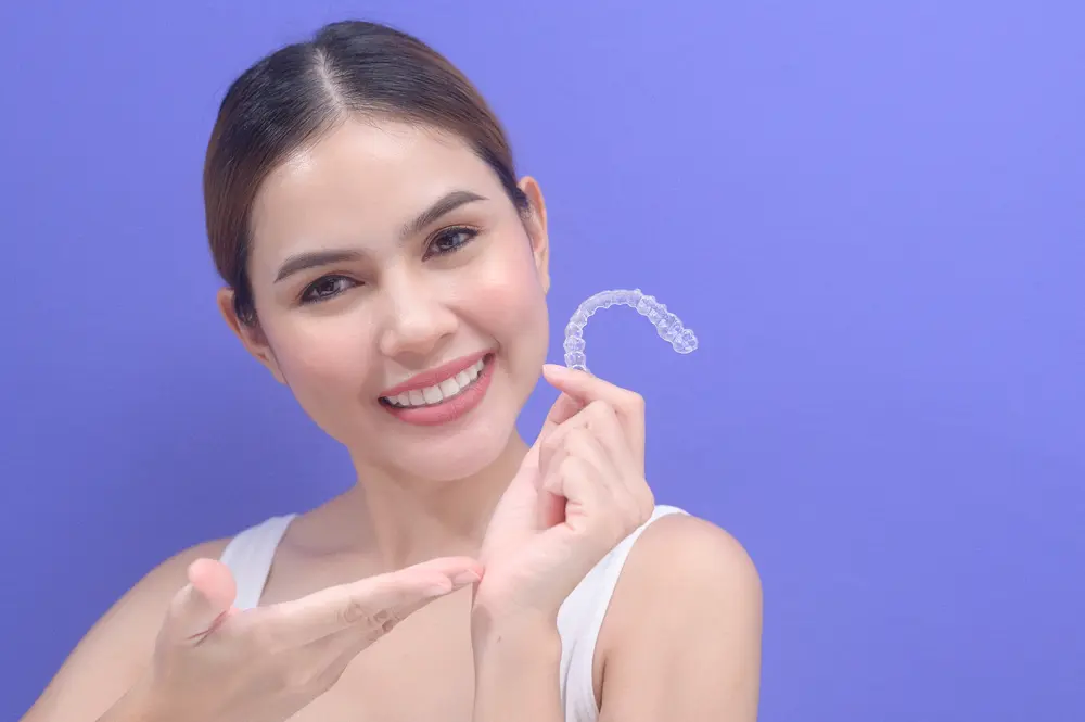 young smiling woman holding invisalign clear aligners - Can Invisalign Fix Overbite in Bakersfield and Tehachapi, CA.