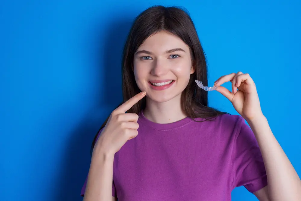 young woman holding invisalign clear aligners pointing her teeth - Can Invisalign Fix Overbite in Bakersfield and Tehachapi, CA.