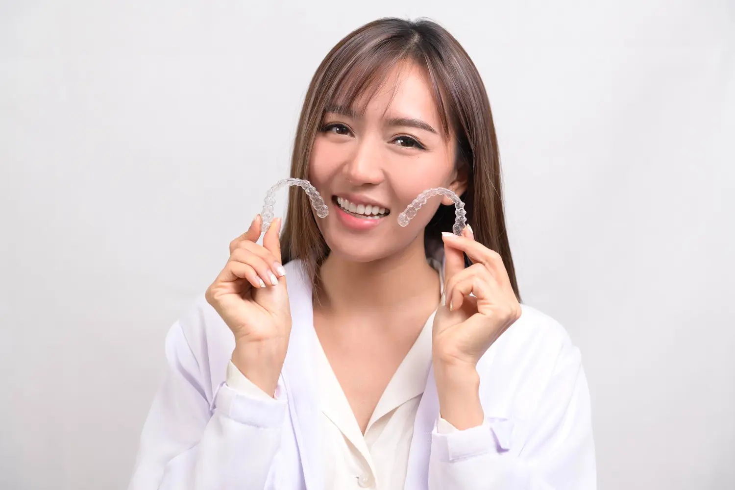 A woman in a white coat smiles, holding Invisalign aligners at Gianquinto Orthodontic Arts in Bakersfield, CA