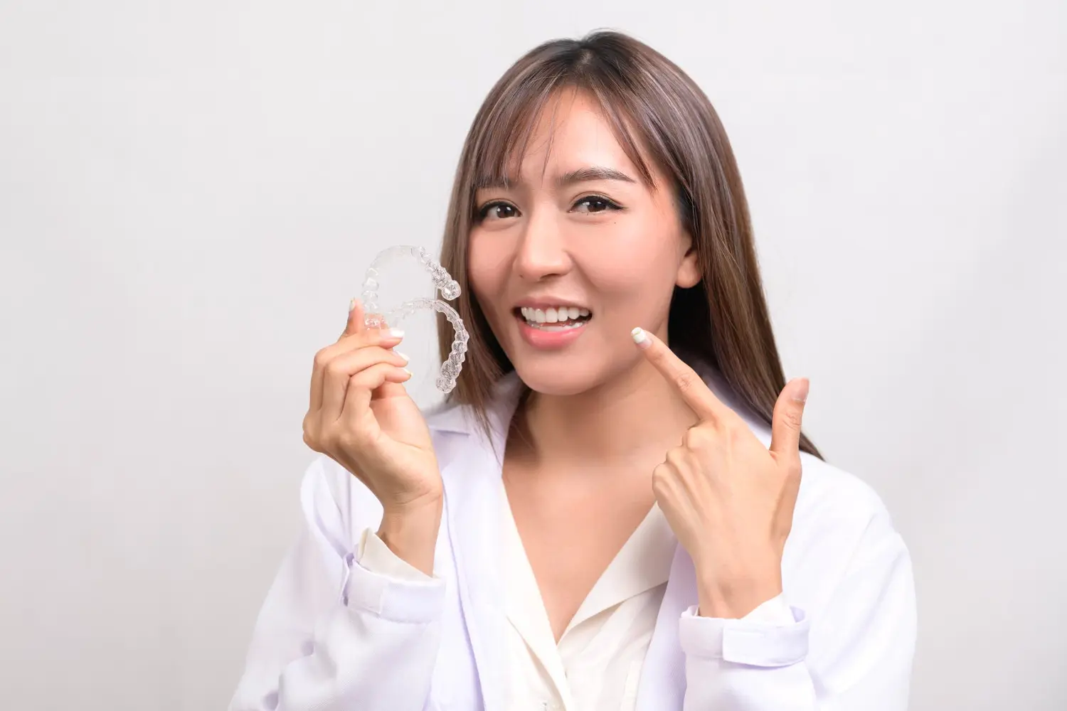 Smiling, a woman in a white coat at Gianquinto Orthodontic Arts in Tehachapi, CA, holds an Invisalign.