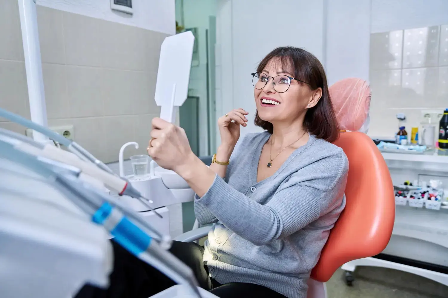 A woman smiles in a dental chair, admiring her reflection after adult orthodontics at Gianquinto Orthodontic Arts in Bakersfield, Tehachapi or Mammoth Lakes, CA