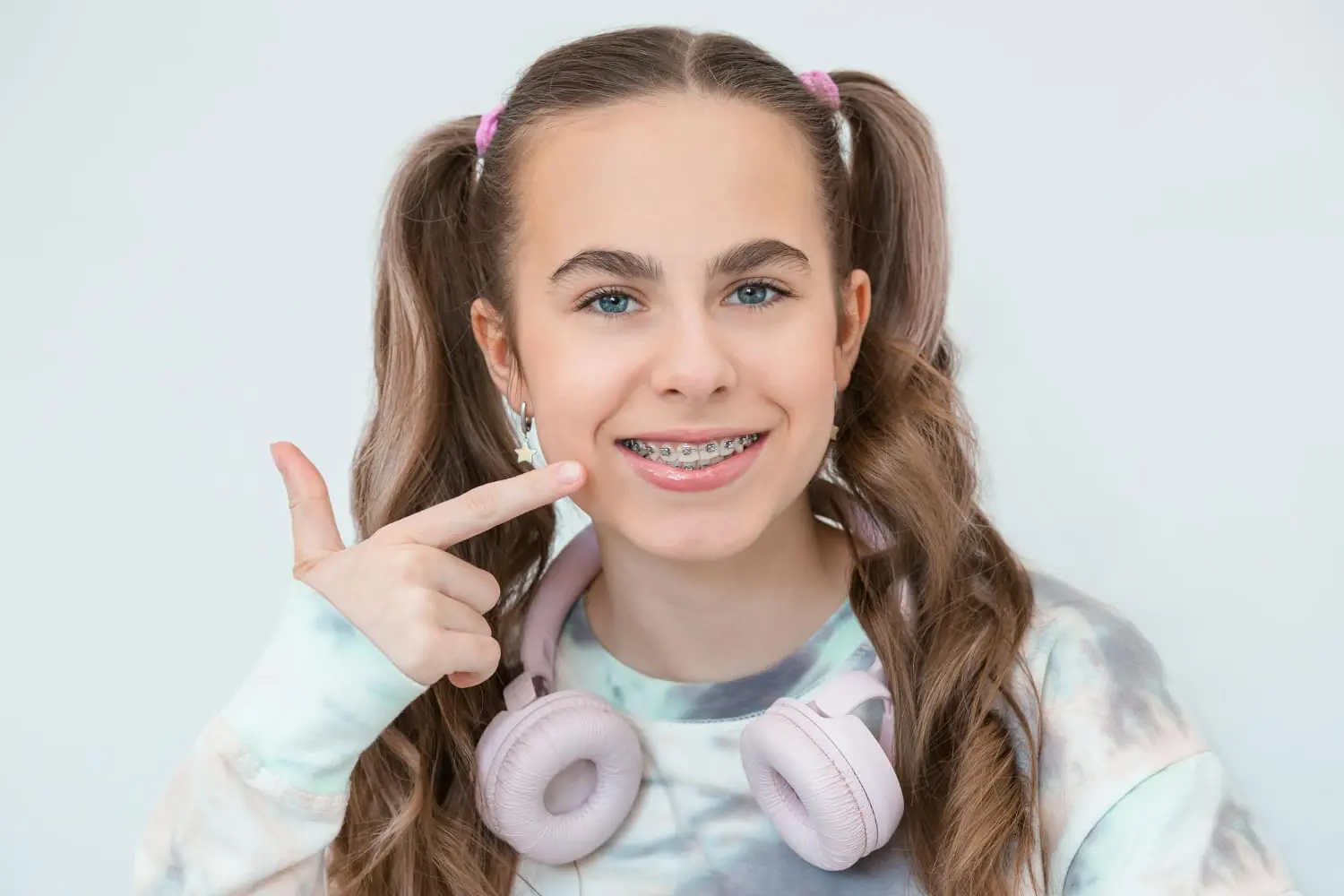 Smiling teen girl with brown hair in pigtails points to her braces, promoting Gianquinto Orthodontic Arts in Bakersfield, CA