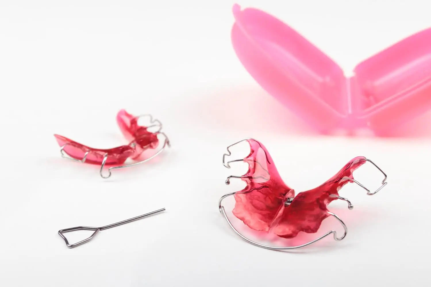 Displayed on a white surface are two red retainers, a metal key, and pink case used from Children’s Orthodontist at Gianquinto Orthodontic Arts in Bakersfield, Tehachapi and Mammoth Lakes, CA.