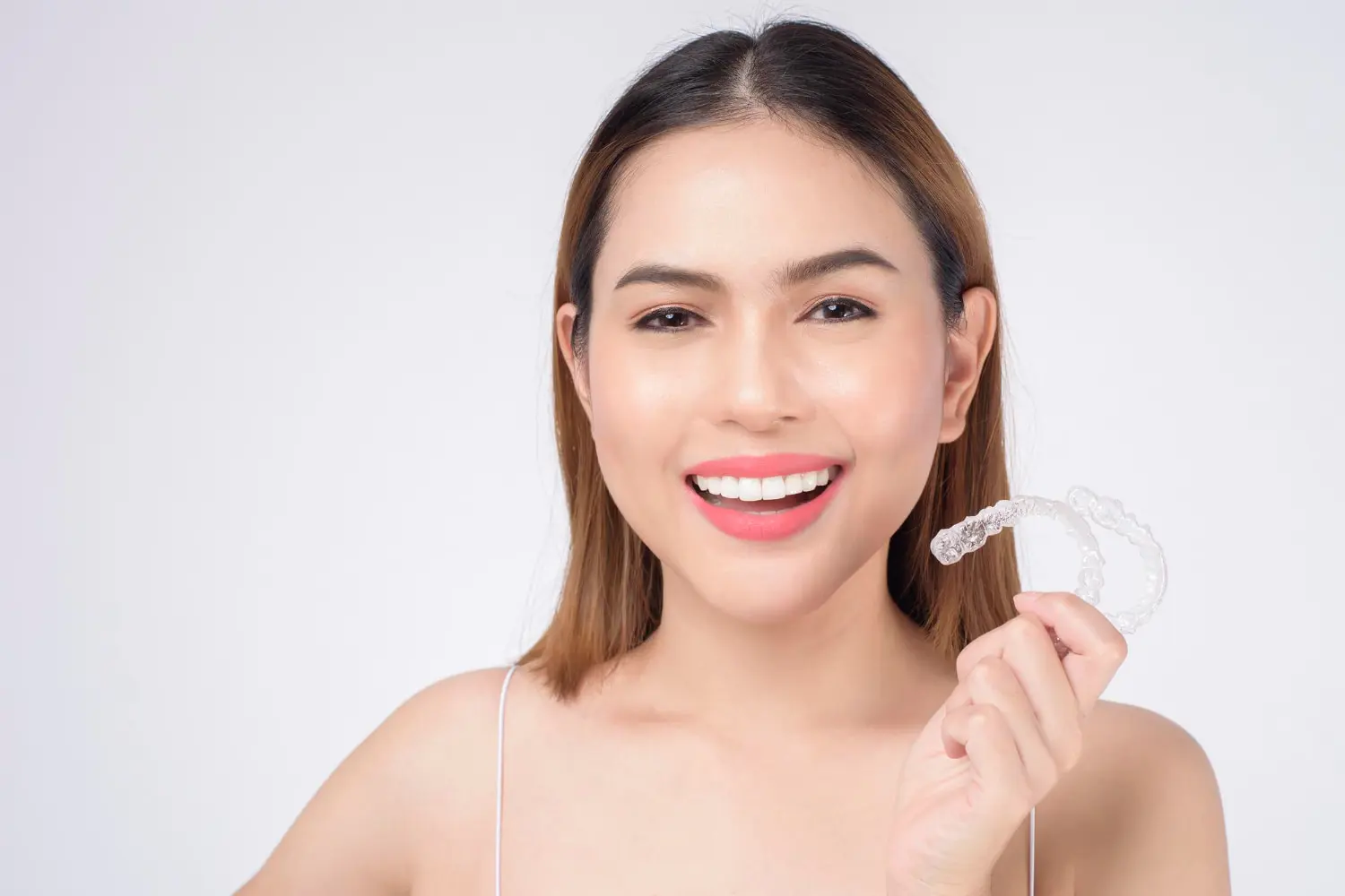 A woman smiles, holding an Invisalign aligner; Gianquinto Orthodontic Arts offers this in Mammoth Lakes, CA.