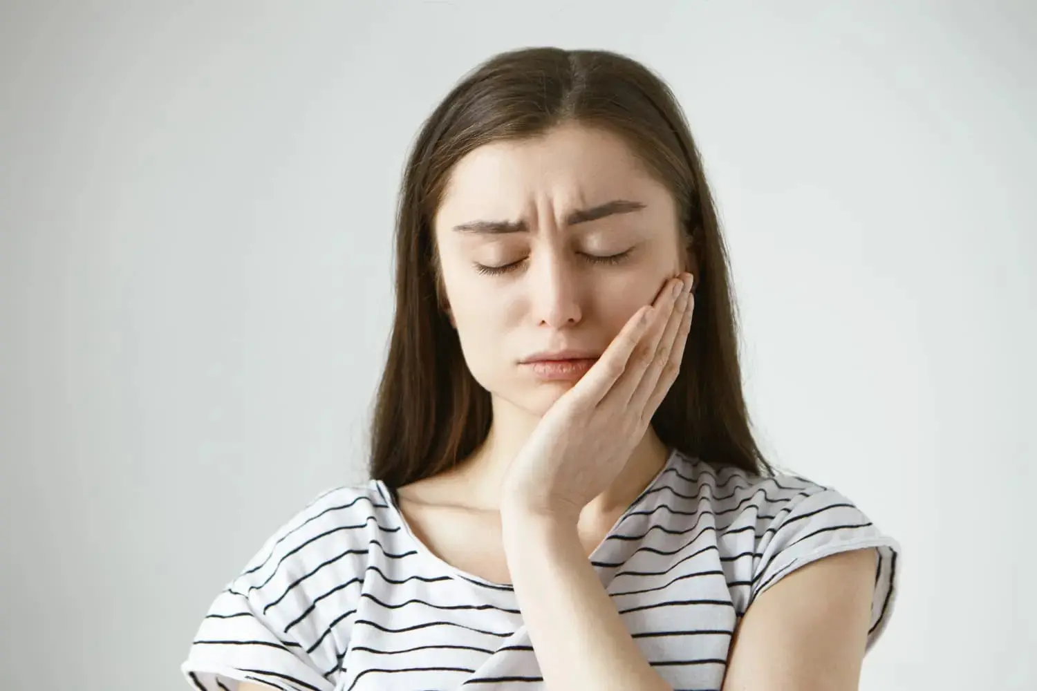 A woman touches her cheek with pain and considers Invisalign vs braces for treatment at Gianquinto Orthodontic Arts in Bakersfield, Tehachapi, and Mammoth Lakes, CA
