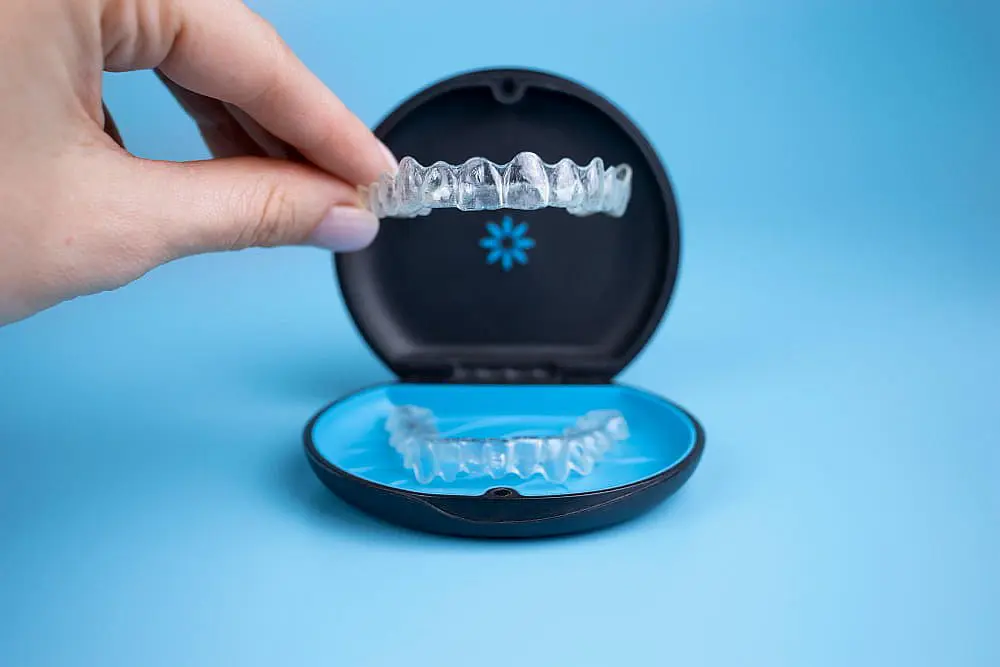 A hand holds an Invisalign clear aligner above an open case with dental insurance from Gianquinto Orthodontic Arts in Bakersfield, Tehachapi, or Mammoth Lakes, CA
