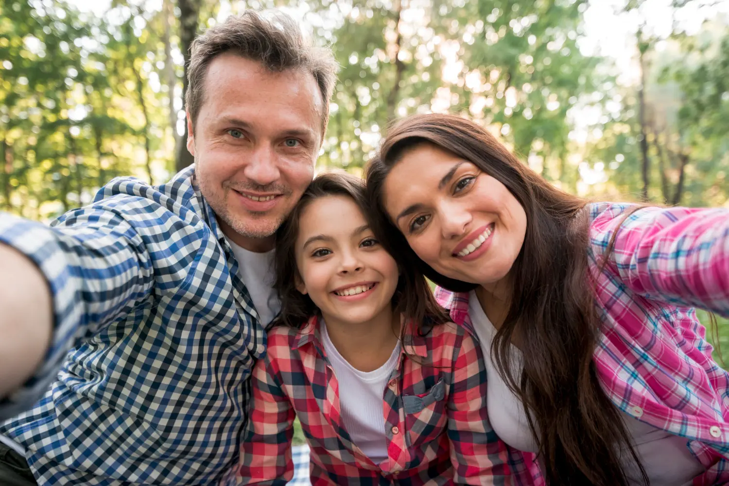 A smiling family in plaid poses outdoors with trees, considering Invisalign vs Braces for Children and adults at Gianquinto Orthodontic Arts in Bakersfield, Tehachapi or Mammoth Lakes, CA.