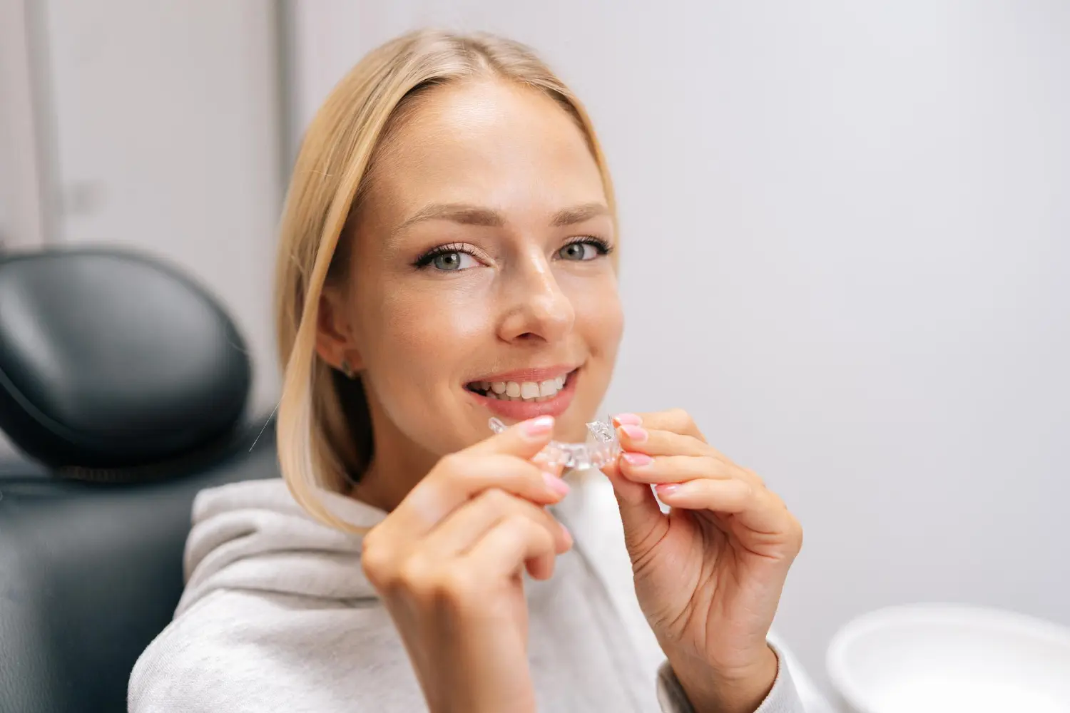 Smiling woman in a dental chair holds an Invisalign clear aligner, and learning In Network Provider Availability for Orthodontic Treatment at Gianquinto Orthodontic Arts in Bakersfield, Tehachapi or Mammoth Lakes, CA.
