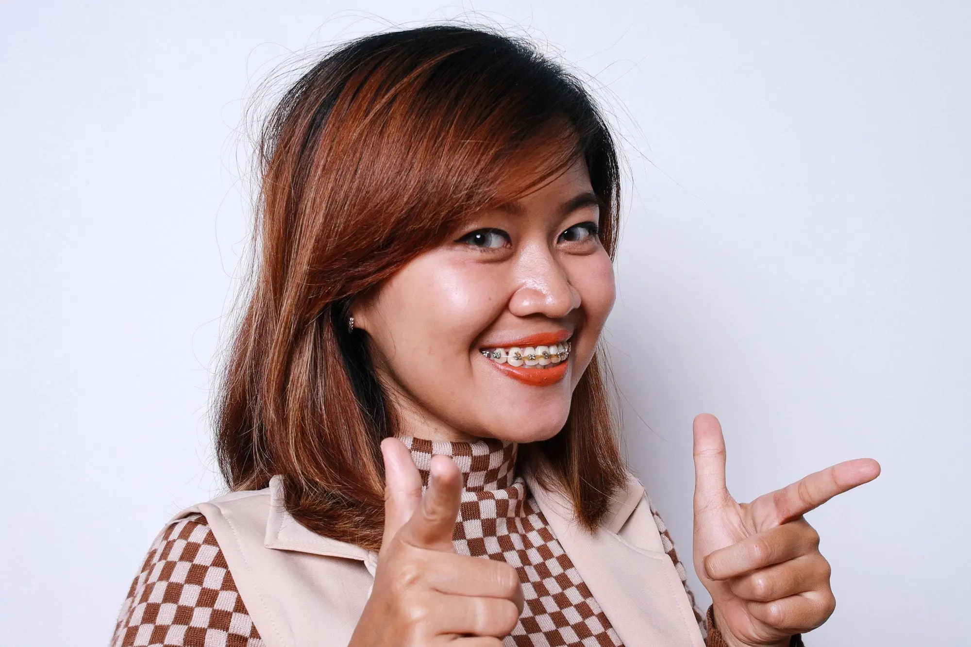Smiling woman with metal braces at Gianquinto Orthodontic Arts in Mammoth Lakes, CA points at camera.