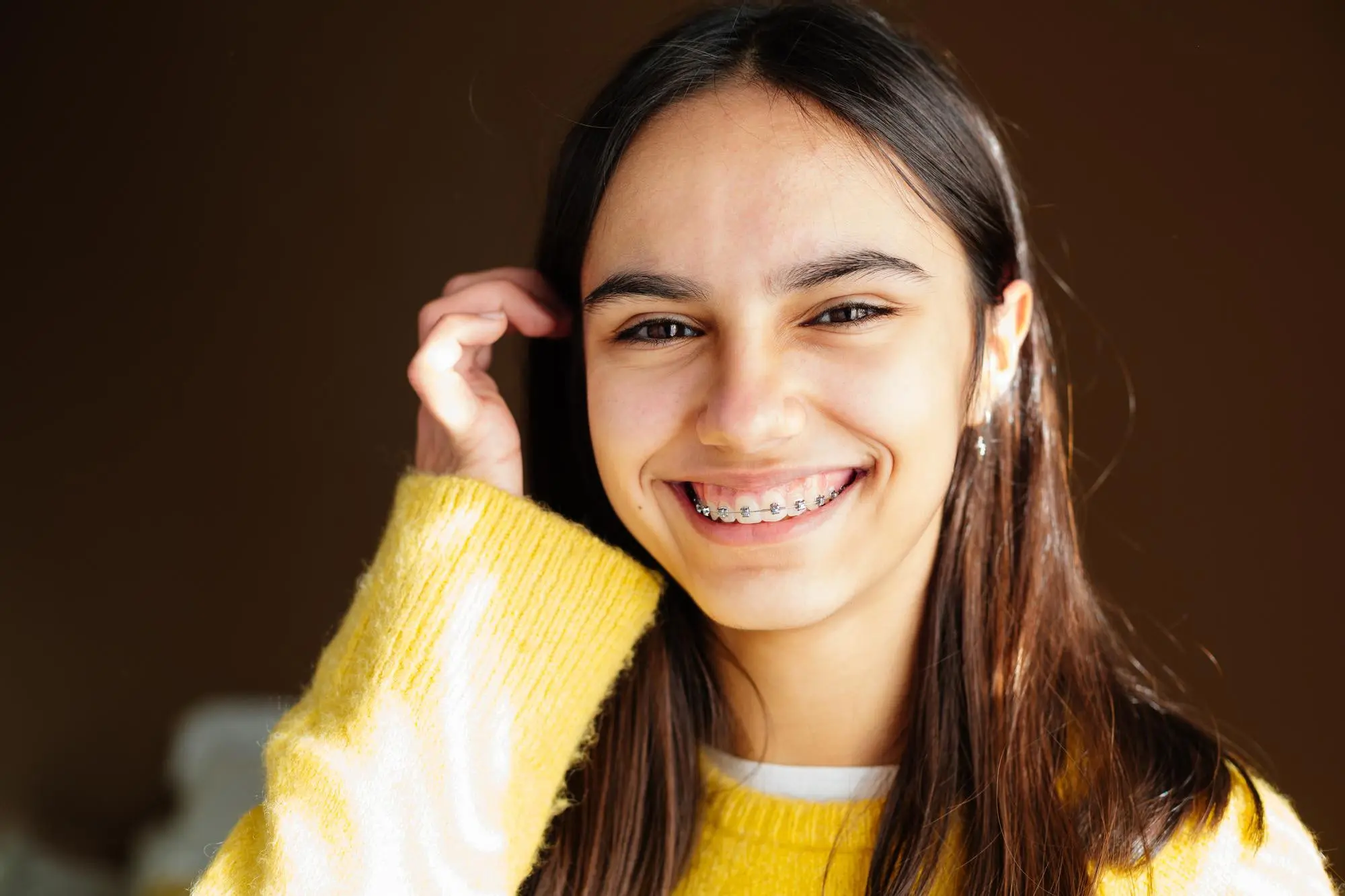 A smiling girl with long brown hair and braces represents the age factor in Orthodontics from Gianquinto Orthodontic Arts in Bakersfield, Tehachapi and Mammoth Lakes, CA.