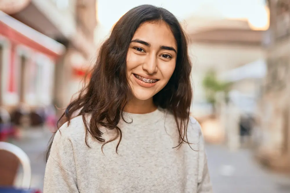 A young person with long hair and metal braces cleans from Gianquinto Orthodontic Arts in Bakersfield, Tehachapi and Mammoth Lakes, CA.