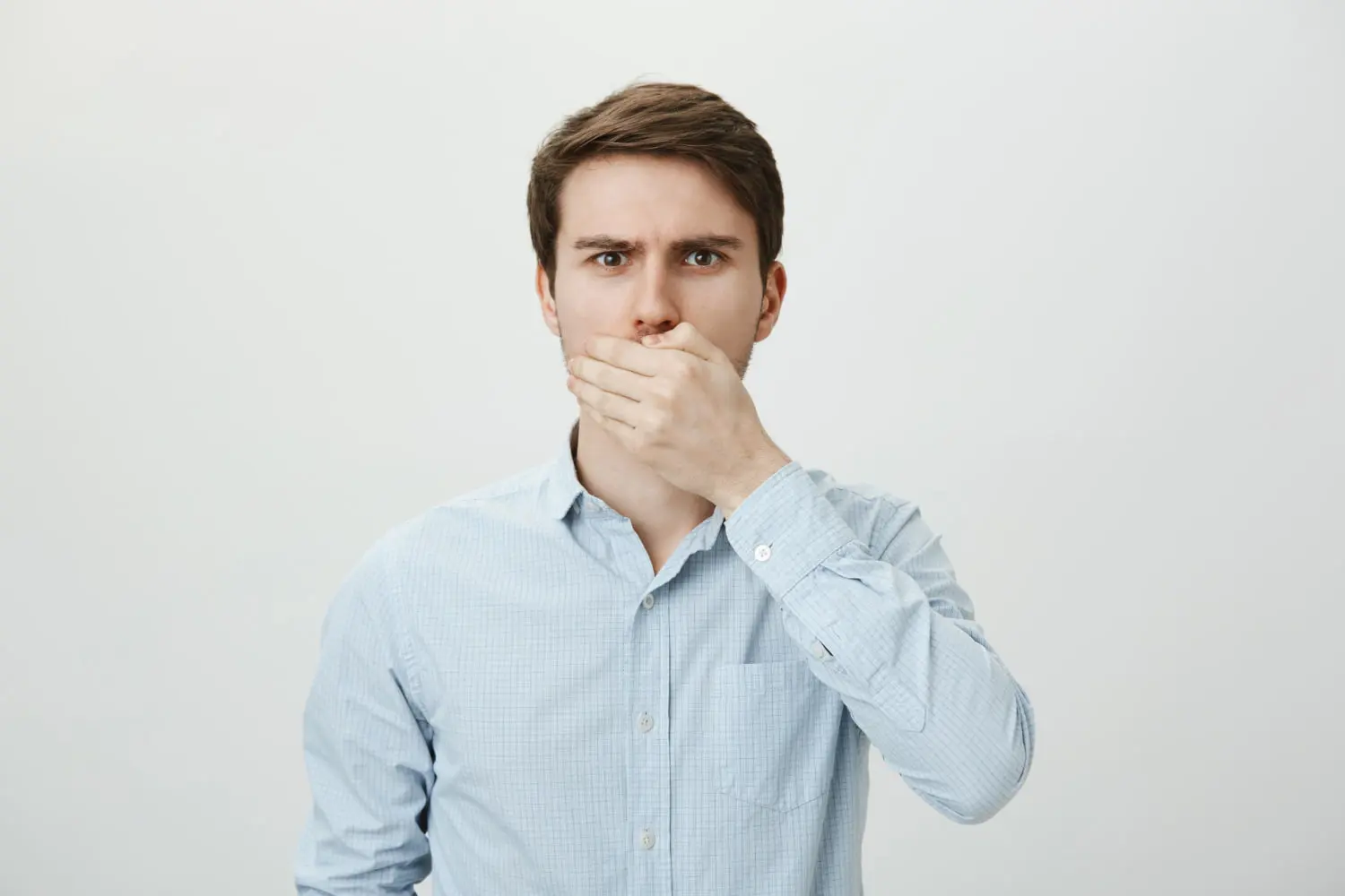 A man in a light blue shirt covers his mouth, reflecting mouth breathing concerns with underbite at Gianquinto Orthodontic Arts in Bakersfield, Tehachapi or Mammoth Lakes, CA