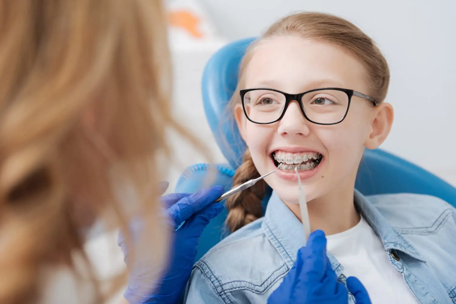 A children's orthodontist at Gianquinto Orthodontic Arts in Bakersfield, Tehachapi and Mammoth Lakes, CA checks a smiling girl's with metal braces as she sits in the chair.