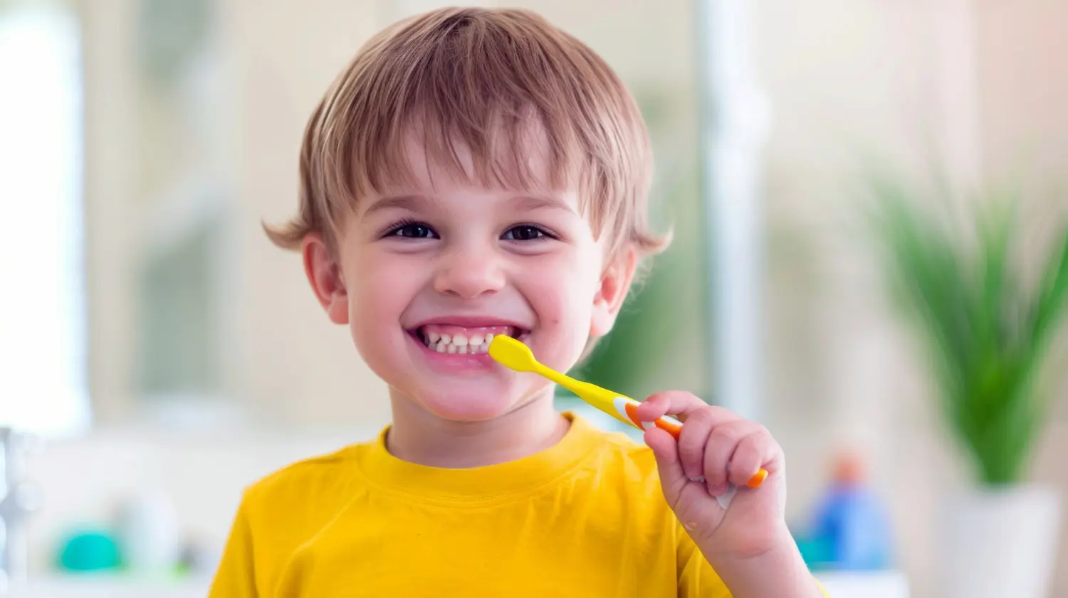 A smiling child brushes teeth with a yellow toothbrush, highlighting Common Orthodontic Issues in Children and trusted Children’s Orthodontist at Gianquinto Orthodontic Arts in Bakersfield, Tehachapi or Mammoth Lakes, CA.