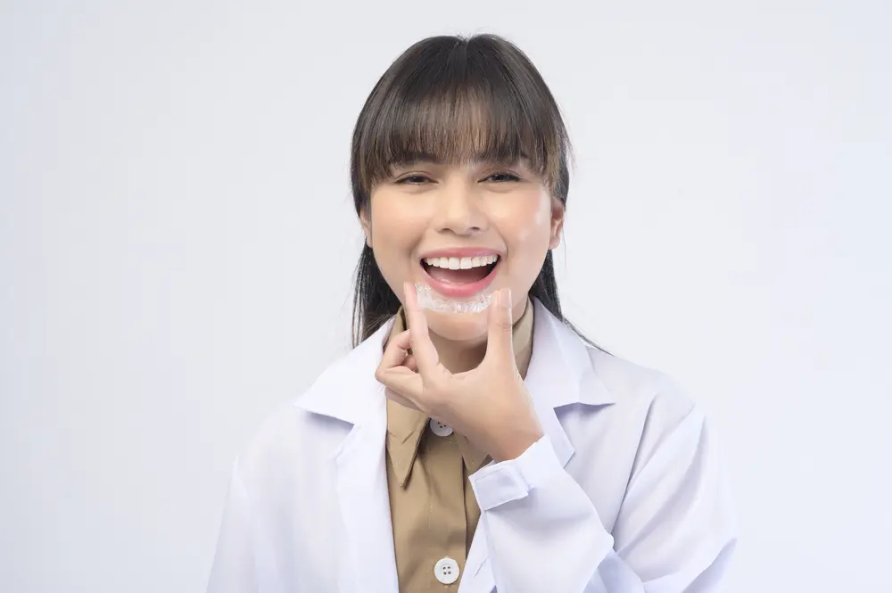 Smiling woman in a white lab coat points to her Invisalign from Gianquinto Orthodontic Arts in Bakersfield, CA