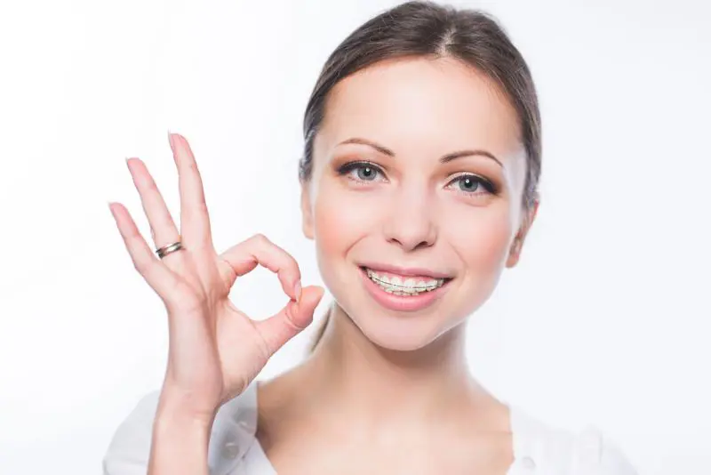 Smiling woman with ceramic braces makes an "OK" gesture, representing Gianquinto Orthodontic Arts in Tehachapi, CA