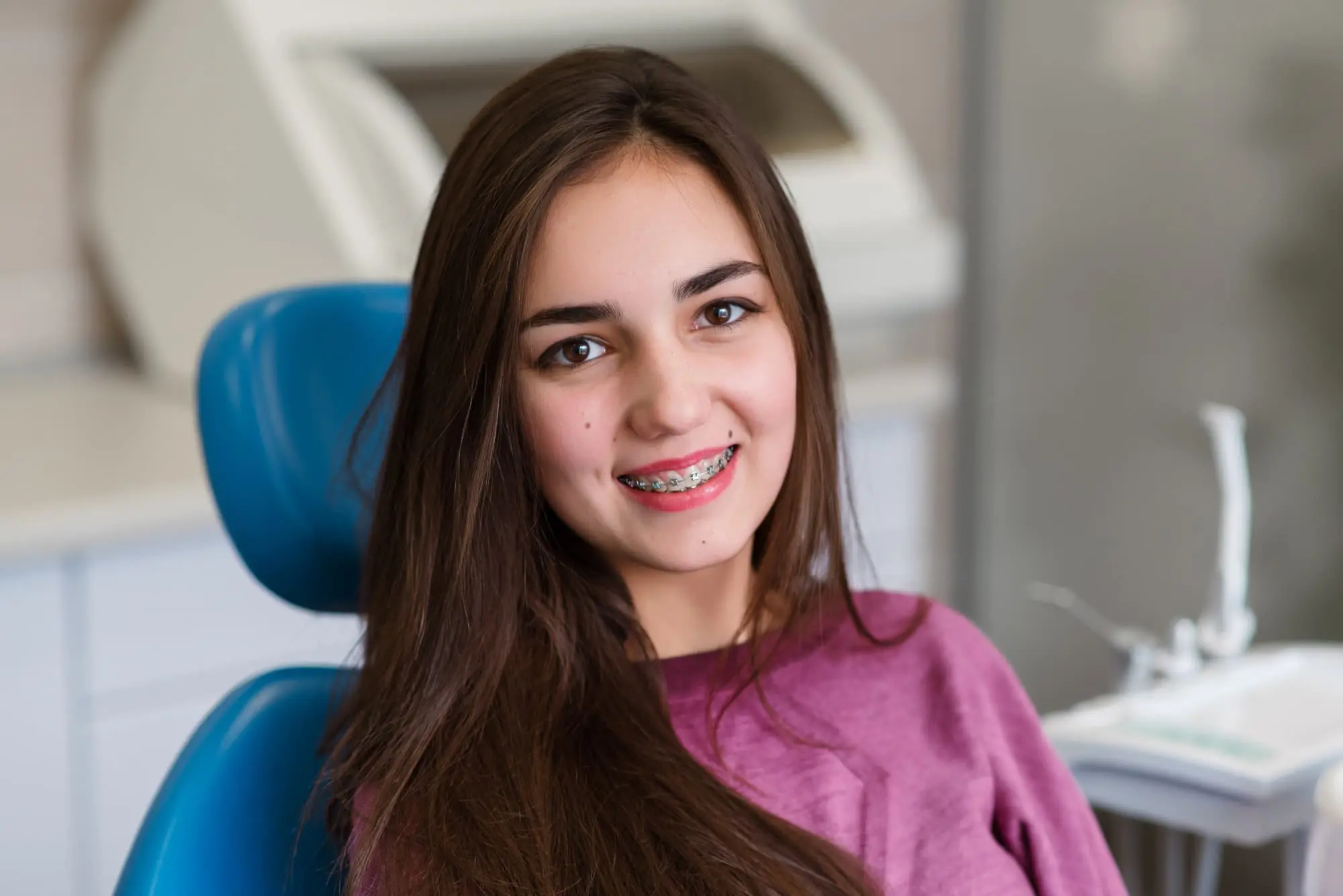At Gianquinto Orthodontic Arts in Bakersfield, Tehachapi or Mammoth Lakes, CA, a young woman with braces smiles in a dental chair ready for braces removal.