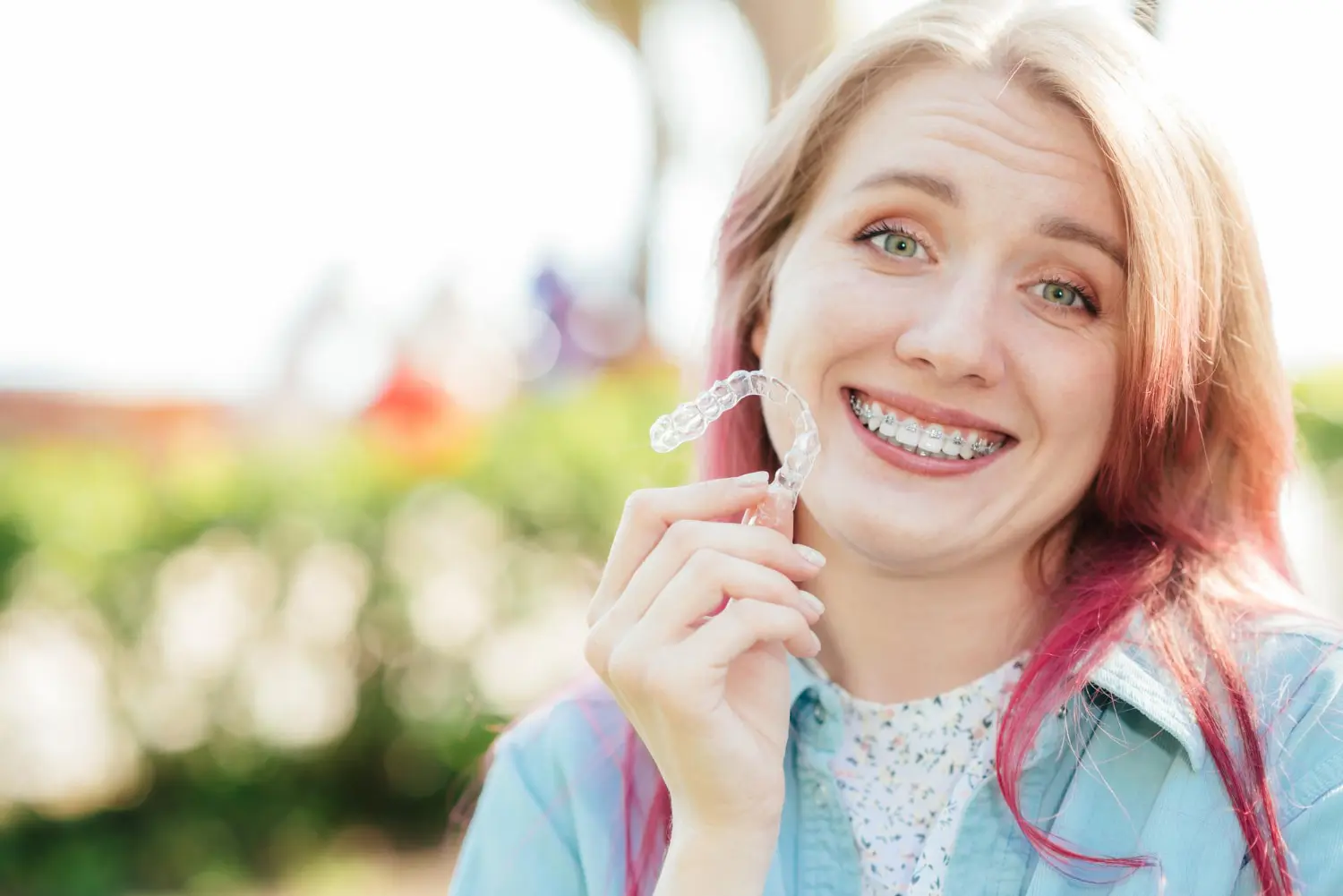 Smiling woman with long curly hair holds an Invisalign aligners at Gianquinto Orthodontic Arts in Bakersfield, CA