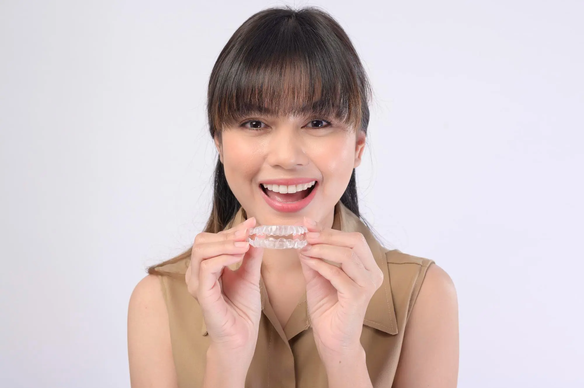 Smiling woman holding a Invisalign clear dental aligner for Gianquinto Orthodontic Arts in Bakersfield, Tehachapi or Mammoth Lakes, CA.