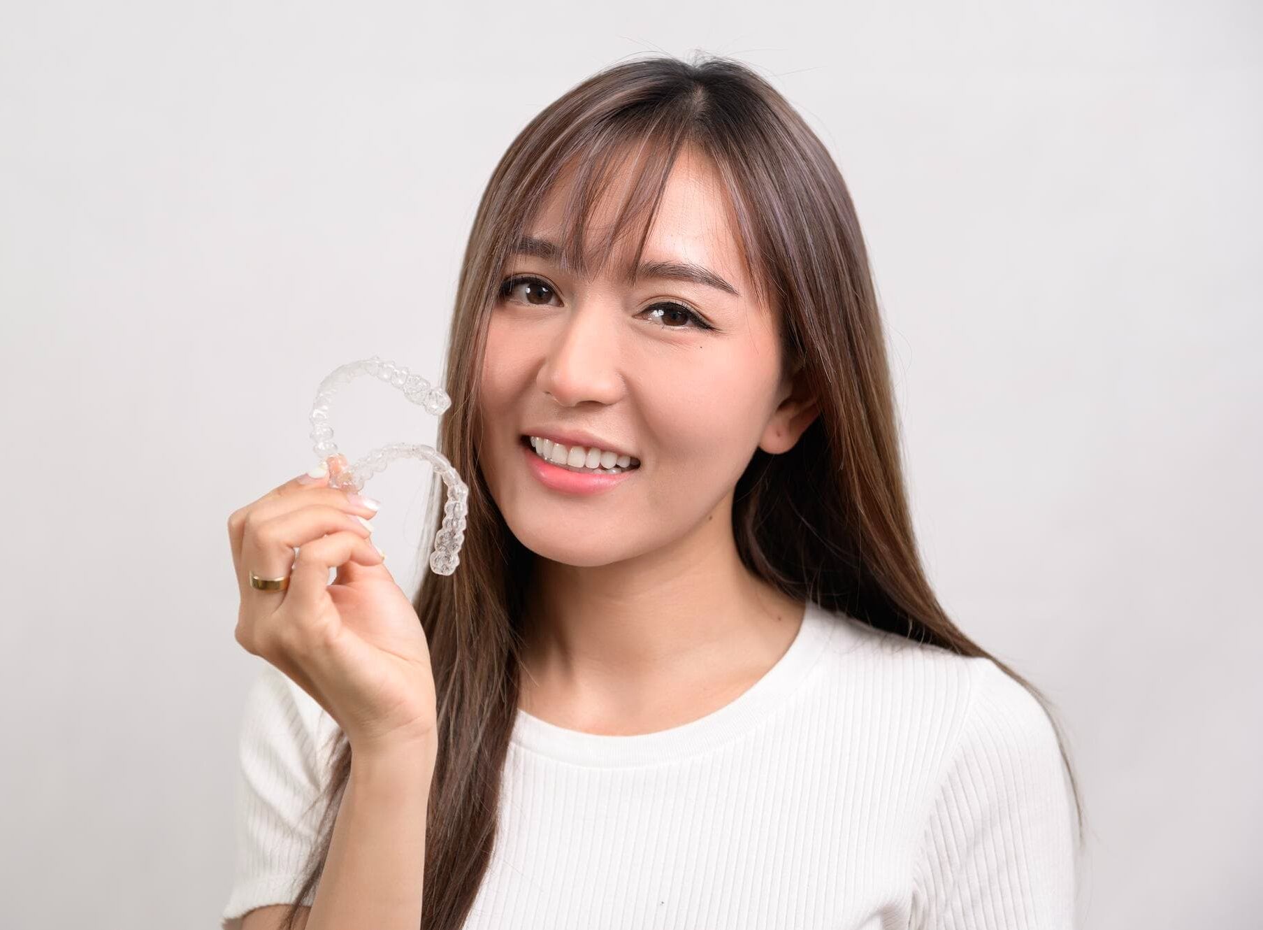 Smiling woman in a white shirt holds Invisalign clear dental aligners promoting Gianquinto Orthodontic Arts in Bakersfield, Tehachapi or Mammoth Lakes, CA